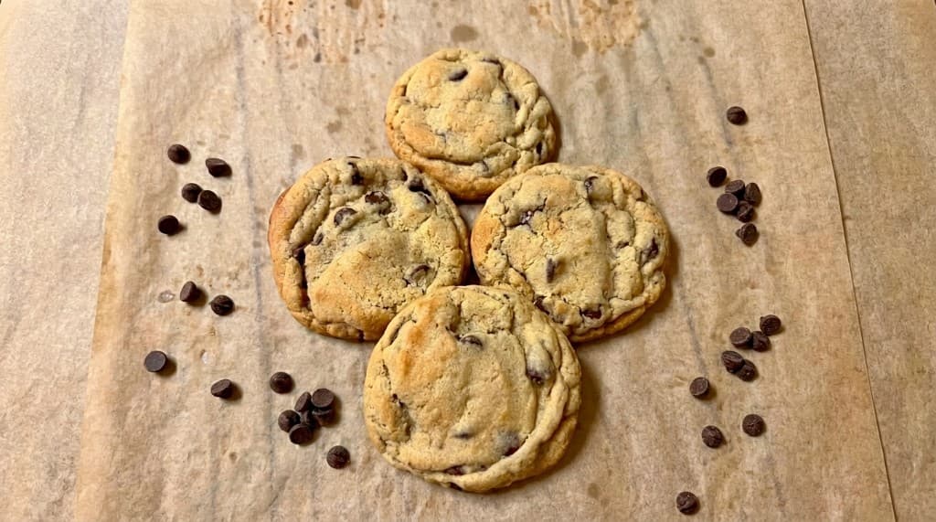 Thick chocolate chip cookies on parchment with loose chips